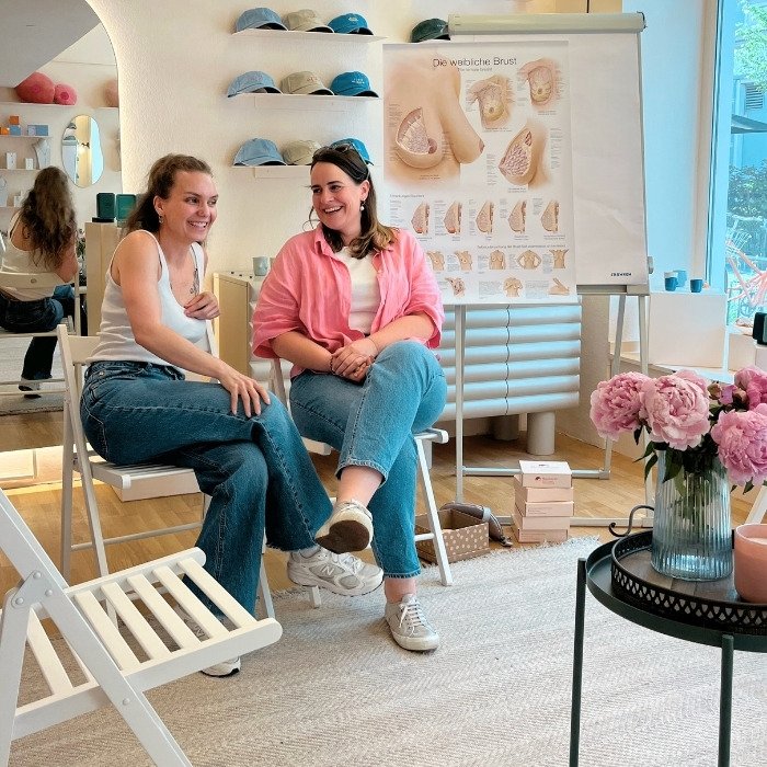 Tatjana und Katharina König sitzen nebeneinander und lächeln sich an.